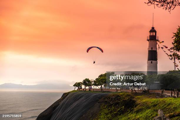 paraglider flying close to the lighthouse of miraflores malecon in lima with stunning sunset view - lima peru stock pictures, royalty-free photos & images