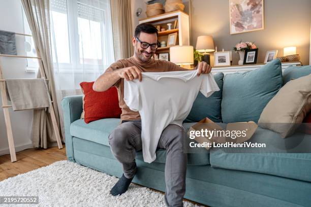 man unboxing clothes after online shopping - hombres de mediana edad fotografías e imágenes de stock