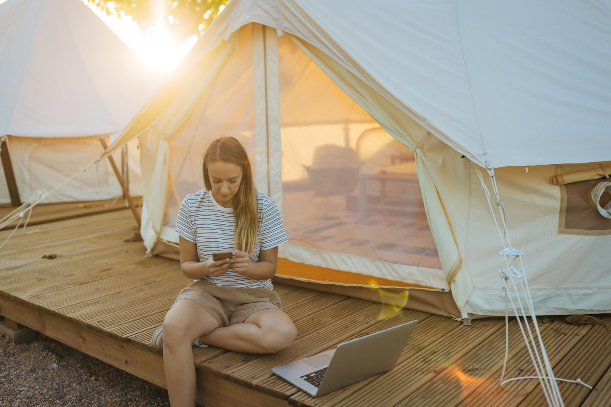 A woman is enjoying her vacation while sitting in front of a glamping tent and using a mobile phone A woman is enjoying her vacation while sitting in front of a glamping tent and using a mobile phone