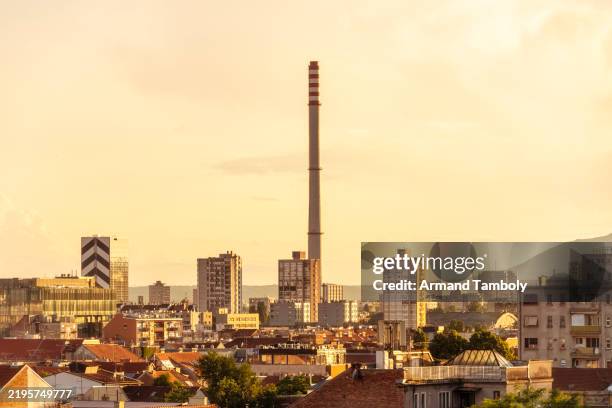 sunset over zagreb city skyline with a tall industrial chimney and residential buildings against a cloudy sky, zageb, croatia - zagreb stock pictures, royalty-free photos & images