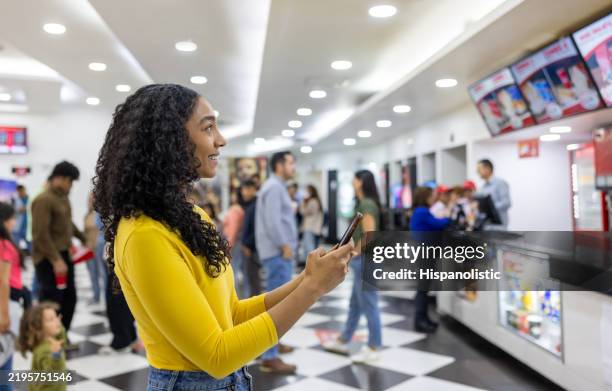 mujer en el cine comprando bocadillos en el puesto de comida usando su teléfono celular - presentación de la película fotografías e imágenes de stock