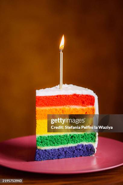 slice of rainbow cake topped with a single lit candle - food coloring stock pictures, royalty-free photos & images