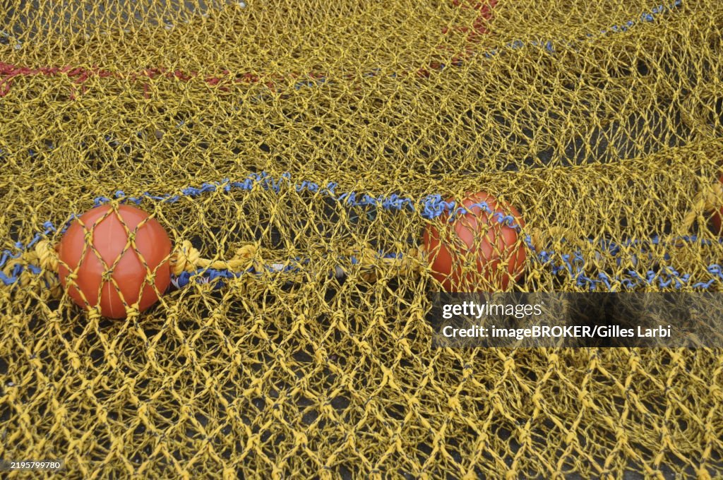 Close-up of a yellow fishing net with red buoys and blue ropes