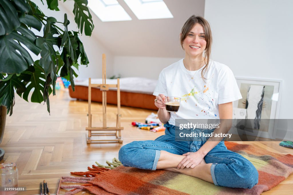 Mujer joven tomando un descanso para tomar café mientras pinta en el estudio de su casa