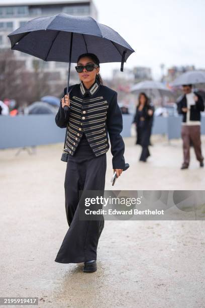 Guest wears black sunglasses, black gold Yves Saint Laurent military jacket, black flowy maxi dress, shiny black platform boots leather shoes,...