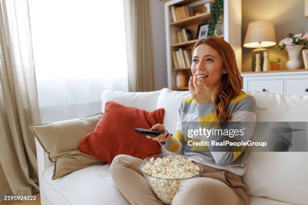 young woman enjoying a movie with popcorn on the sofa at home - serviço de distribuição digital contínua imagens e fotografias de stock