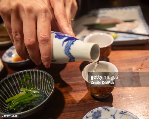 pouring nihonshu (japanese rice wine) at an izakaya - reishu stock pictures, royalty-free photos & images