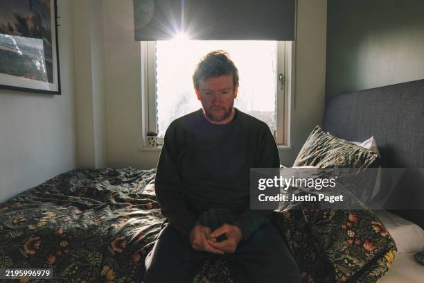 powerful shot of a mature man, sitting on his bed, looking sad - negative emotion - sadness stock pictures, royalty-free photos & images