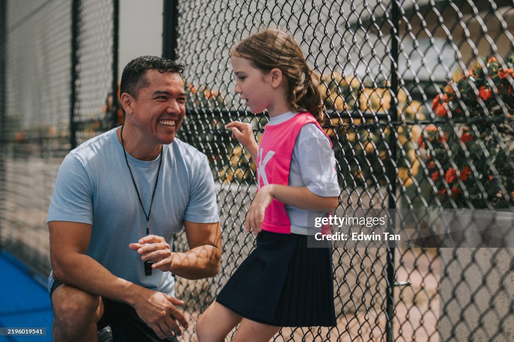 Australian coach bonding to his daughter, young netball team player goal keeper during practice