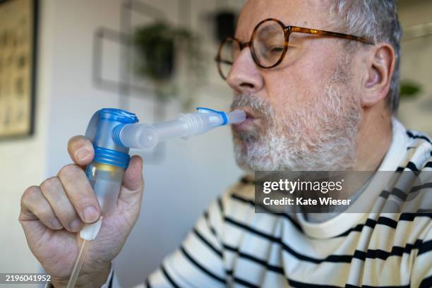 an older man using a nebulizer at home - nebulizer stock pictures, royalty-free photos & images