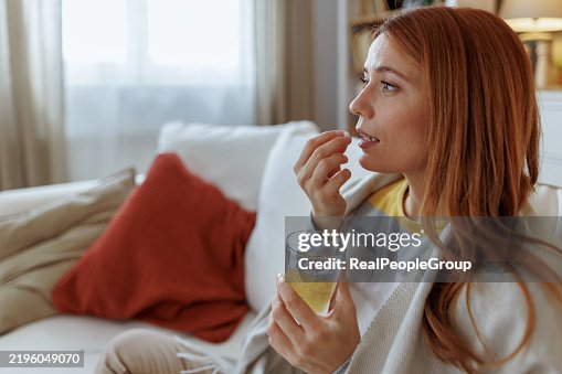 Sick young woman taking a pill and drinking a glass of water on the sofa Sick young woman taking a pill and drinking a glass of water on the sofa