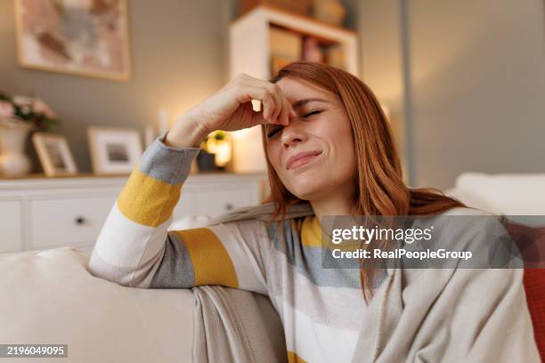 woman suffering from sinus pain while sitting on sofa at home - forehead stock pictures, royalty-free photos & images