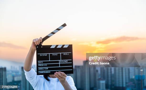 frau hände halten filmschiefer vor dem hintergrund der stadt bei sonnenuntergang himmel - film und rundfunkausrüstung stock-fotos und bilder