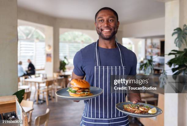 waiter serving food at a restaurant and smiling - ober stockfoto's en -beelden