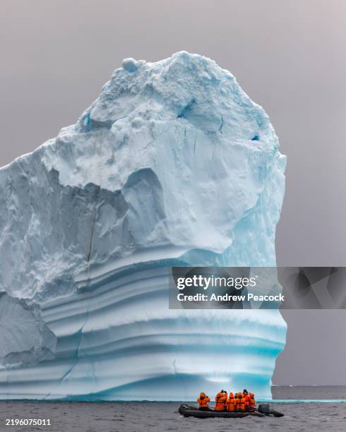 travellers to antarctica on a zodiac cruise beside a huge iceberg. - polar climate stock pictures, royalty-free photos & images