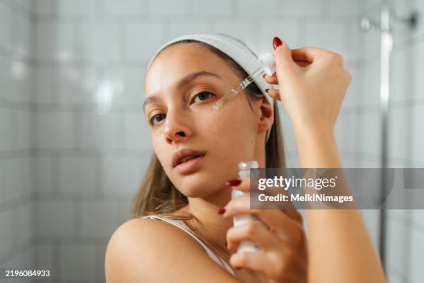 giovane donna che applica il siero per il viso in un bagno moderno - trattamento per la pelle foto e immagini stock