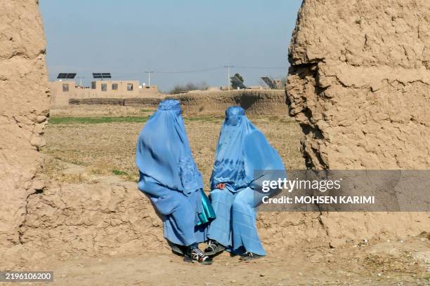 Afghan burqa-clad women sit along a street at Injil district in Herat province on January 30, 2025.