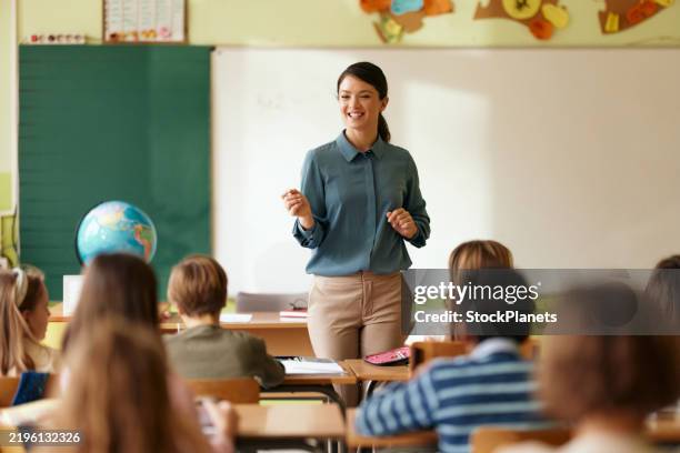 glückliche grundschullehrerin, die ihren schülern in einer klasse eine vorlesung hält. - lehrkraft stock-fotos und bilder
