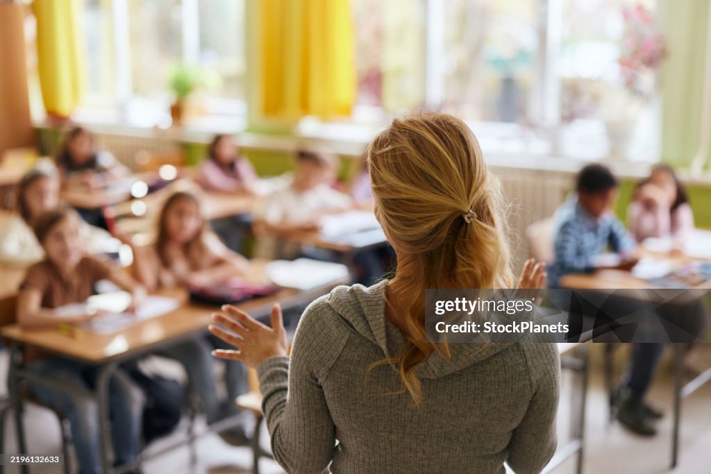 Rückansicht eines Grundschullehrers, der über eine Vorlesung in einer Klasse spricht.