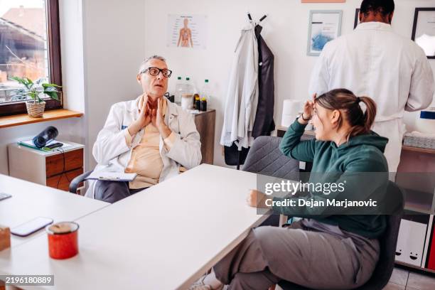 doctor talking to a female patient in office checking her health status with medical assistant around - ordination stock pictures, royalty-free photos & images