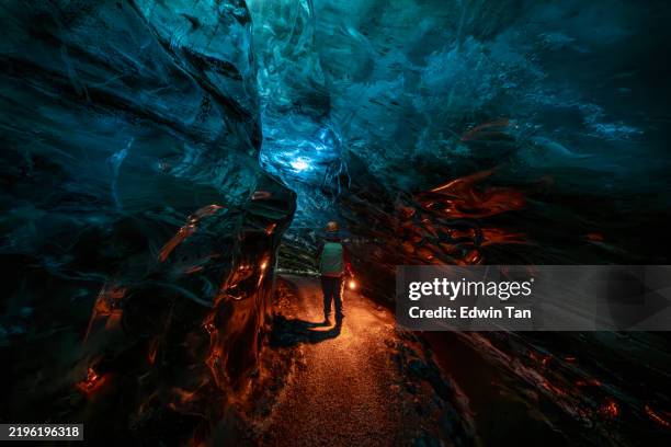 vue arrière asiatique chinois femme mûre explorant la grotte de glace, islande tenant une lampe électrique - paysage enchanteur photos et images de collection