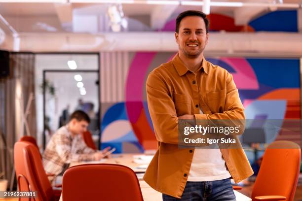homme d’affaires confiant souriant les bras croisés dans un bureau moderne - représentation masculine photos et images de collection