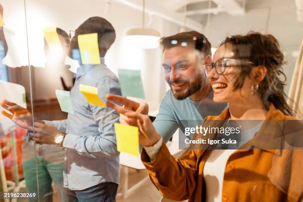 coworkers using sticky notes on glass wall during a brainstorming session - scrum stock pictures, royalty-free photos & images