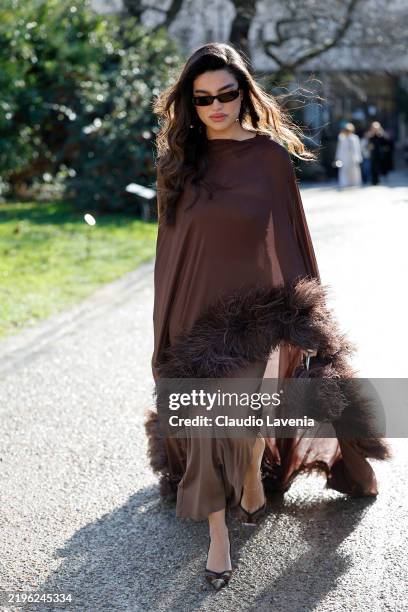 Guest wears brown long dress, matching sheer cape with feathers, brown heels, outside Georges Hobeika, during Haute Couture Spring-Summer 2025 as...