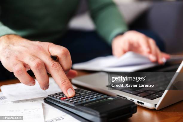 mature man calculating home expenses using calculator and laptop at home - rechenmaschine stock-fotos und bilder