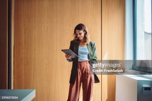confident young professional using tablet in a modern office environment - businesswoman stock pictures, royalty-free photos & images