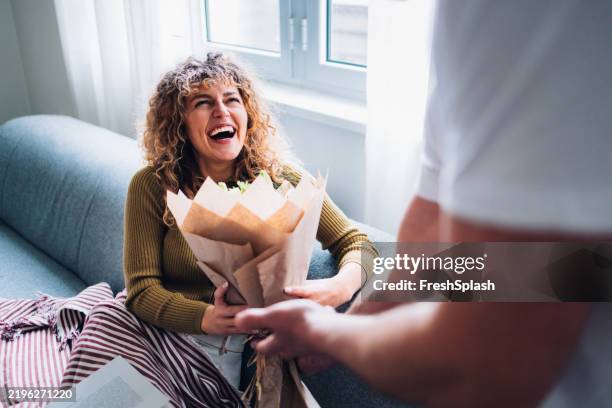 excited woman receiving flowers while relaxing on a comfortable couch - receiving stock pictures, royalty-free photos & images