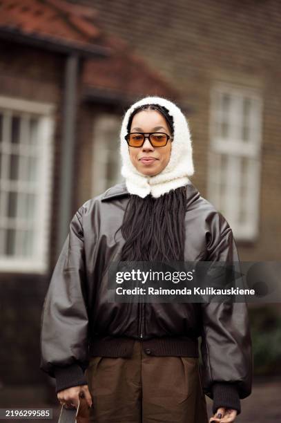 Amaka Hamelijnck wears wide brown pants, dark brown leather jacket, white hat outside the OpéraSport show during the Copenhagen Fashion Week...
