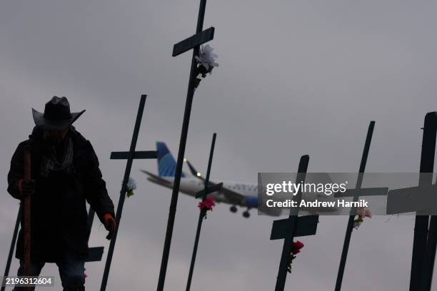 An airplane lands at Reagan National Airport as Roberto Marquez from Dallas, Texas, digs a hole for a cross as part of a memorial for the victims of...