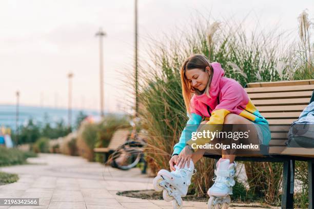 young woman putting on roller skates in a park - skaten stockfoto's en -beelden