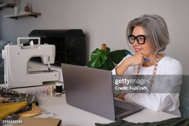 designer de mode senior travaillant sur un ordinateur portable - industrie de la mode photos et images de collection