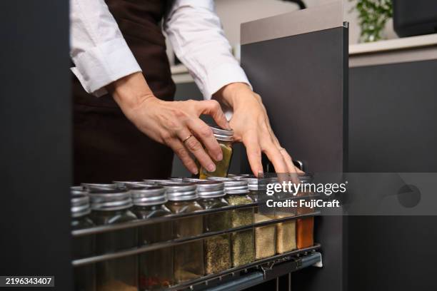 woman taking a jar of spices from a kitchen cabinet - specerij stockfoto's en -beelden