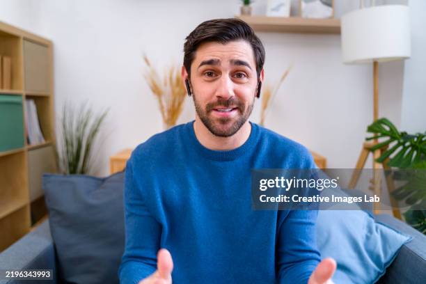 man having a video call from home, wearing wireless earphones - videoconferenza foto e immagini stock