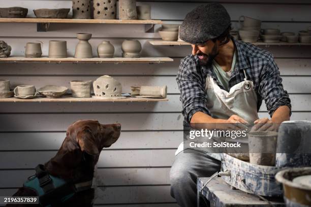 man creating pottery with dog watching - modern manhood stock pictures, royalty-free photos & images