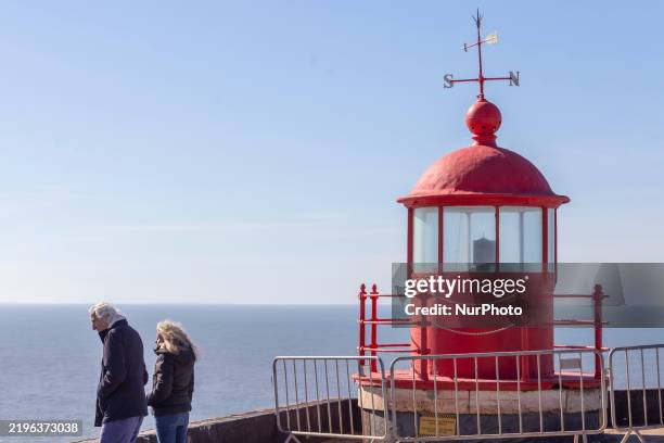 People visit the lighthouse at Praia do Norte on January 31, 2025 in Nazare, Portugal, Strong swells and high winds from Storm Ivo persist in Nazare,...