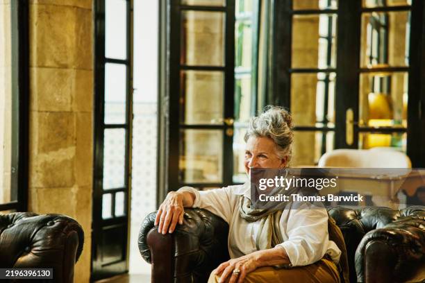 medium wide shot smiling senior woman relaxing in lounge of luxury hotel - vecchio saggio foto e immagini stock