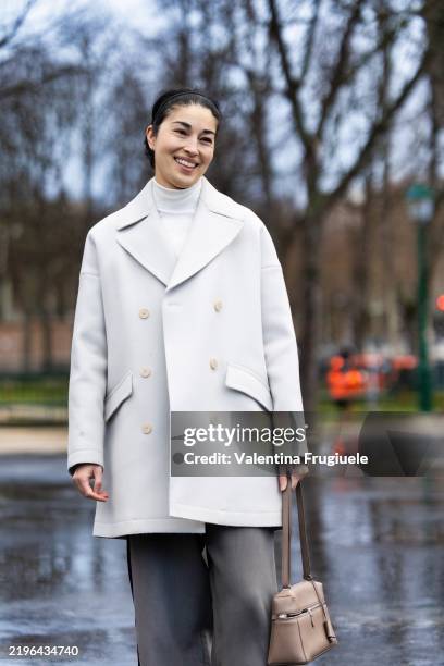 Caroline Issa wears a white turtle neck sweater, a white coat, denim grey wide leg trousers and a beige leather bag outside Chanel show during Haute...