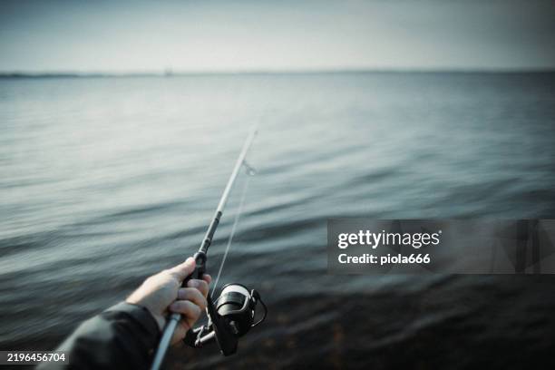 man spinning fishing in the sea with a rod, from the rocks - cana de pesca imagens e fotografias de stock