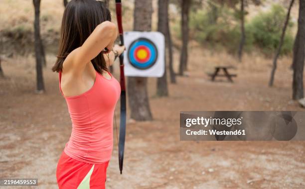 archer aiming at target board with bow and arrow at forest - longbow stock pictures, royalty-free photos & images