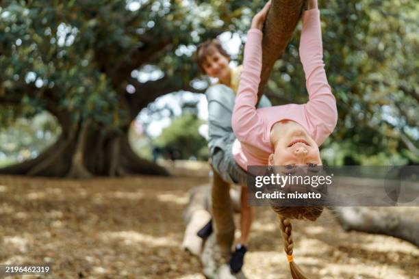 ragazza in posa per la macchina fotografica mentre è appesa a testa in giù su un ramo di un albero - giochi per bambini foto e immagini stock