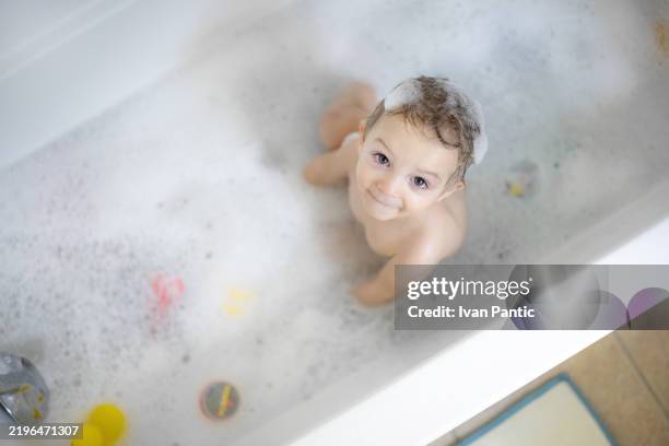 young child smiling while playing in a bubbling bathtub - bathhouse stock pictures, royalty-free photos & images