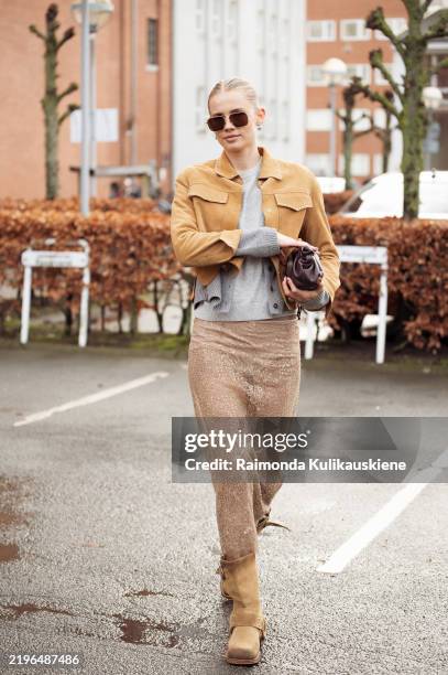 Andrea Steen wears sheer beige skirt, beige suede shoes, grey top and sweater, brown suede jacket and sunglasses outside the Nicklas Skovgaard show...