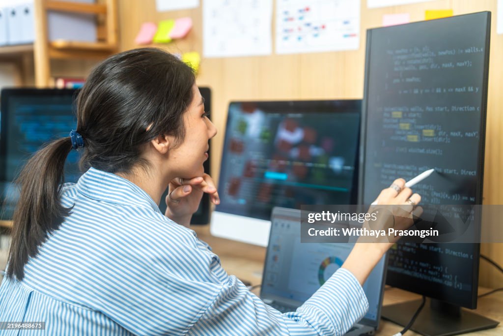 Young Programmer Analyzing Code on Multiple Computer Screens in Office Environment