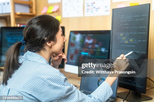 Young Programmer Analyzing Code on Multiple Computer Screens in Office Environment Young Programmer Analyzing Code on Multiple Computer Screens in Office Environment