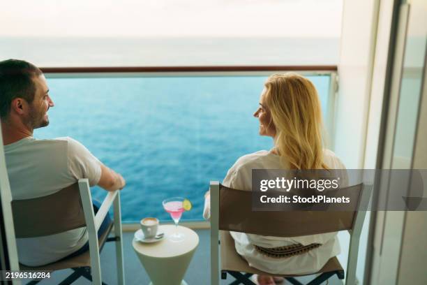 a couple is sitting on a deckchair on the balcony of the cruise ship and enjoying their drinks - cruise vacation stock pictures, royalty-free photos & images