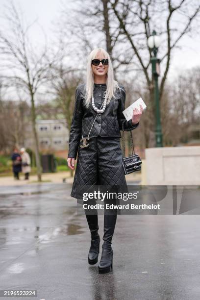 Guest wears black sunglasses, shiny black quilted Chanel leather jacket, white ball Chanel necklace, silver Chanel brooch, silver Chanel crossbody...